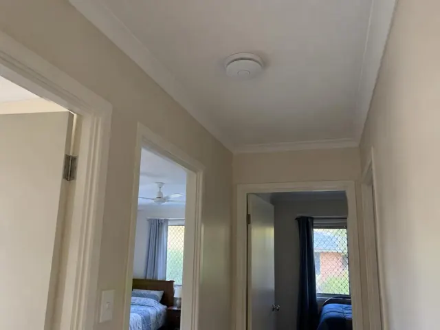 Hallway ceiling smoke alarm in a beige home with open doorways and bedrooms visible in Merrimac