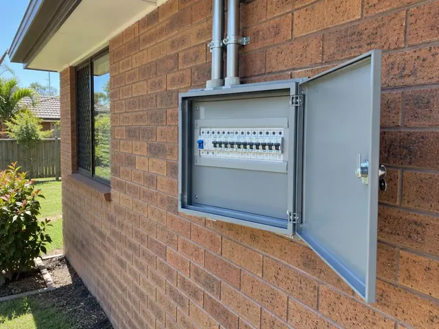 Open exterior switchboard on a brick house wall with conduit above in Worongary